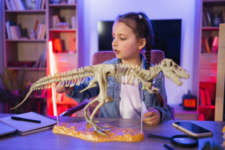 Caucasian child making model of tyrannosaurus out of bones in evening at home.