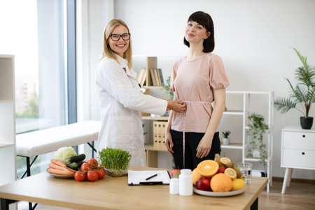 Mature woman in doctors coat finding out waist length of female patient.の写真素材