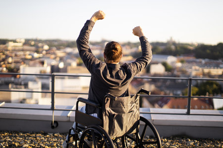 Man in wheelchair raising arms in triumph overlooking cityの写真素材