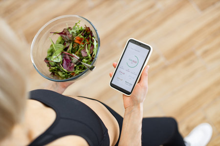 Woman tracking calories on smartphone while eating healthy saladの写真素材