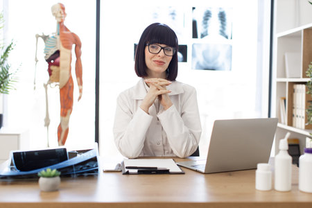 Female doctor sitting at desk in medical office with x-raysの写真素材