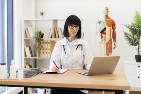 Female doctor taking notes while working on laptop in office