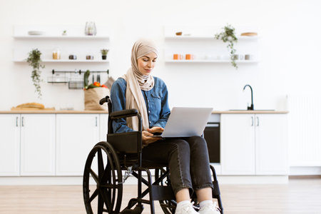 Muslim woman in wheelchair using laptop at home officeの写真素材