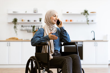 Muslim woman in wheelchair on phone at home kitchenの写真素材