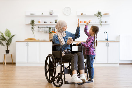 Muslim mother in wheelchair with daughter using smartphoneの写真素材