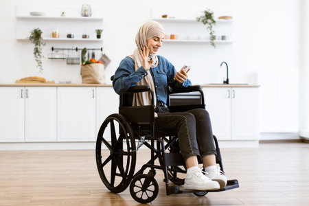 Muslim woman in wheelchair using smartphone at home kitchenの写真素材