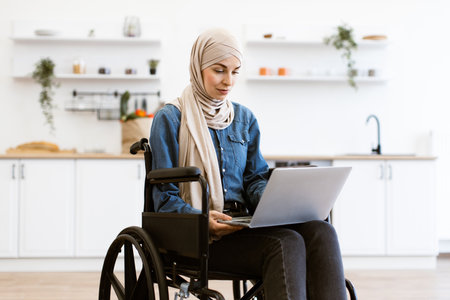 Muslim woman in wheelchair using laptop at homeの写真素材