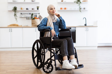 Muslim woman in wheelchair relaxing at home in modern kitchenの写真素材