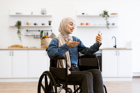 Muslim woman in wheelchair using smartphone at home kitchenの写真素材