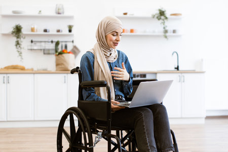 Muslim woman in wheelchair working from home on laptopの写真素材