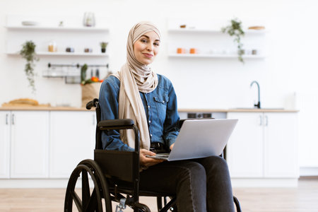 Muslim woman in wheelchair working on laptop at homeの写真素材