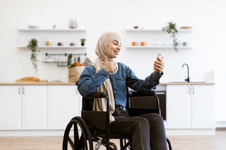 Muslim woman in wheelchair taking selfie at home kitchenの写真素材