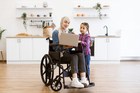 Woman with young girl using a laptop in kitchenの写真素材