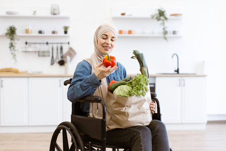 Muslim woman in wheelchair with fresh vegetables in kitchenの写真素材