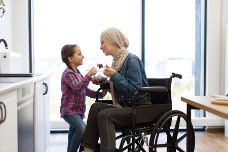 Muslim mother in wheelchair and daughter eating fresh salad together