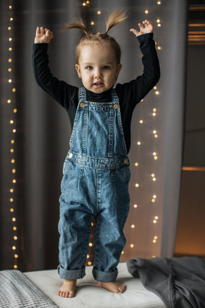 Cute toddler in denim overalls raising arms with joyの写真素材