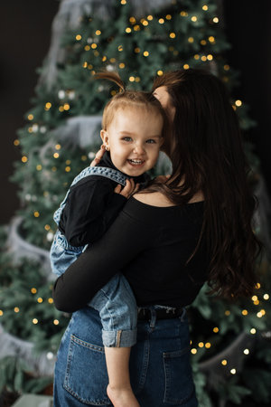 Mother embraces her young daughter by Christmas treeの写真素材