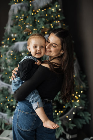 Mother embraces her young daughter by Christmas treeの写真素材