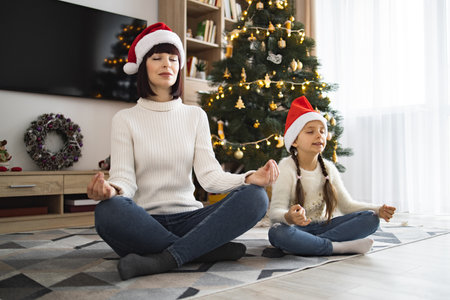 Mother and daughter meditating by the Christmas tree in festive hatsの写真素材