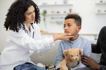 Female doctor examining boys lymph nodes at home with concerned dadの写真素材