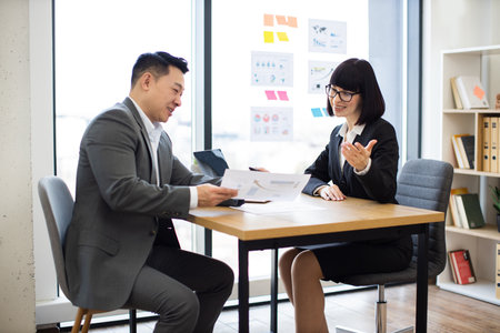 Asian businessman shows report to Caucasian businesswoman in modern officeの写真素材