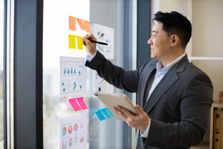 Asian businessman analyzing charts on window with digital tabletの写真素材