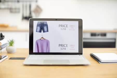 Open laptop displaying online store selling clothes with discounts. Various apparel items like jeans and sweaters shown with prices. Scene suggests modern online shopping and digital commerce.の写真素材