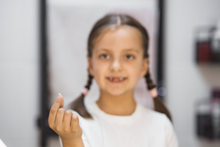 Portrait of young girl showing freshly fallen baby tooth while looking into mirror in bathroom, expressing pride and excitement.の写真素材