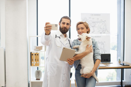 Young male veterinarian and female dog owner with dog posing for selfie in clinic. Captures veterinary professionalism and bond between owner, pet.の写真素材