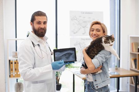 Veterinarian holding x-ray results discussing diagnosis with woman holding her cat in arms at animal clinicの写真素材
