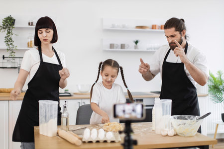 Caucasian family cooking together in kitchen, creating content as bloggers, dancing and smiling. Emphasizing strong bond through culinary activity, mixing fun and culinary skillsの写真素材