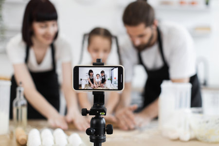 Caucasian family recording cooking tutorial. Parents and daughter knead dough on kitchen table.の写真素材