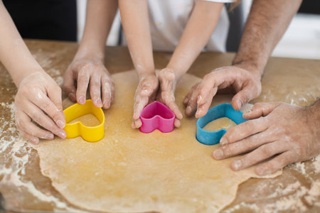 Family preparing cookies with hands using heart-shaped molds on rolled dough, showcasing teamwork.の写真素材