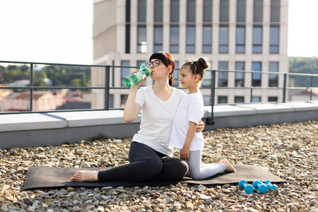 Mother with daughter doing rooftop fitness activities, focusing on hydration. Emphasizes bonding, health.の写真素材