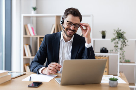 Smiling adult male wearing suit using laptop during business communication in office setting.の写真素材