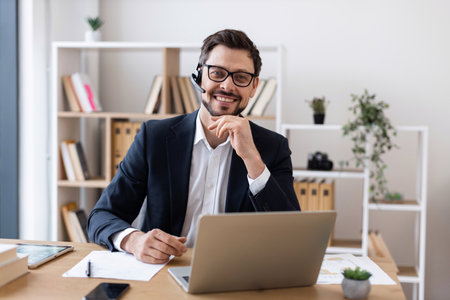Smiling adult male wearing suit using laptop during business communication in office setting.の写真素材