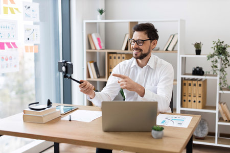 Smiling young adult male professional workplaces creating business content with smartphone in office. Displays productive working environment, successful interaction, digital recording.の写真素材