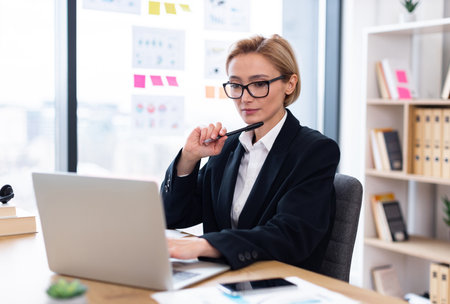 Businesswoman working on laptop at desk in office, analyzing report. Focused, professional, and diligent, portraying concepts of business analysis, professionalism, and office workの写真素材