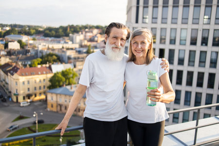 Elderly man and woman standing on rooftop smiling after morning exercise, displaying energy, health and companionship. Modern urban setting with fitness and wellness concept.の写真素材