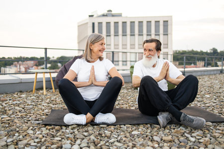 Senior man and woman practicing yoga in relaxed on urban rooftop. Promotes wellness, mindfulness, and active lifestyle among elderly. Depicts harmony, fitness, and companionship through yoga posture.の写真素材