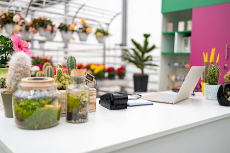 A beautifully arranged florist shop interior featuring plants, a laptop, and payment equipment on a white table.の写真素材
