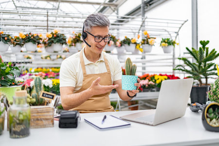 A florist on a video call, showing a cactus to a customer. The shop has a large selection of flowers.の写真素材