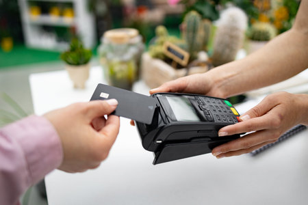 A person pays for purchases at a florist shop by using a credit card with a contactless payment...