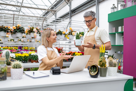 Two florists discuss a plant at the sales counter in a plant shop filled with various flowers and plants for sale.の写真素材