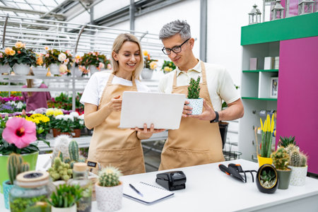 A florist and a customer checking a laptop while at a sale table in the shop. The woman is holding the laptop, and the man is holding a potted plant.の写真素材