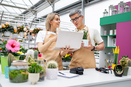A florist and a shop owner, both Caucasian, look at a laptop. The image captures a scene of a sale table.の写真素材