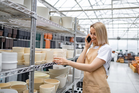 A friendly shop assistant talks on her phone, surrounded by various flowerpots in a bright shop.の写真素材