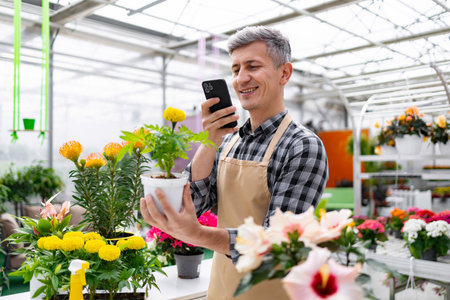 A man in a greenhouse takes a photo of a plant with his smartphone.の写真素材