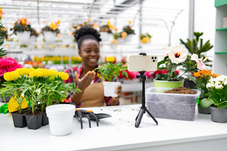 A woman broadcasts from a garden center. She is surrounded by flowers and plants.の写真素材