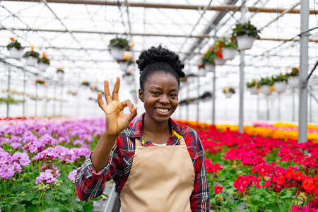 Smiling African woman in a greenhouse, giving the okay gesture.の写真素材